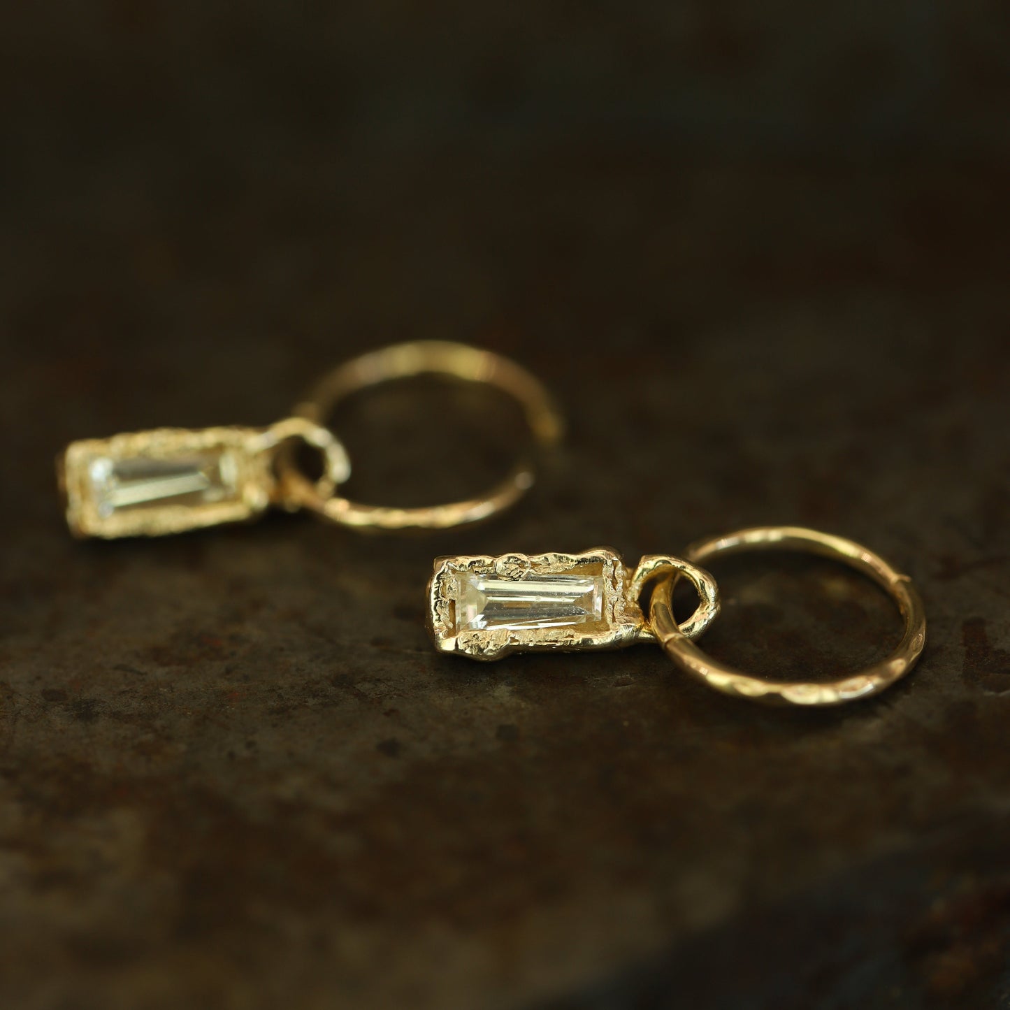 Ellis Mhairi Cameron - Gold hoop earrings with baguette gemstones on a dark brown background