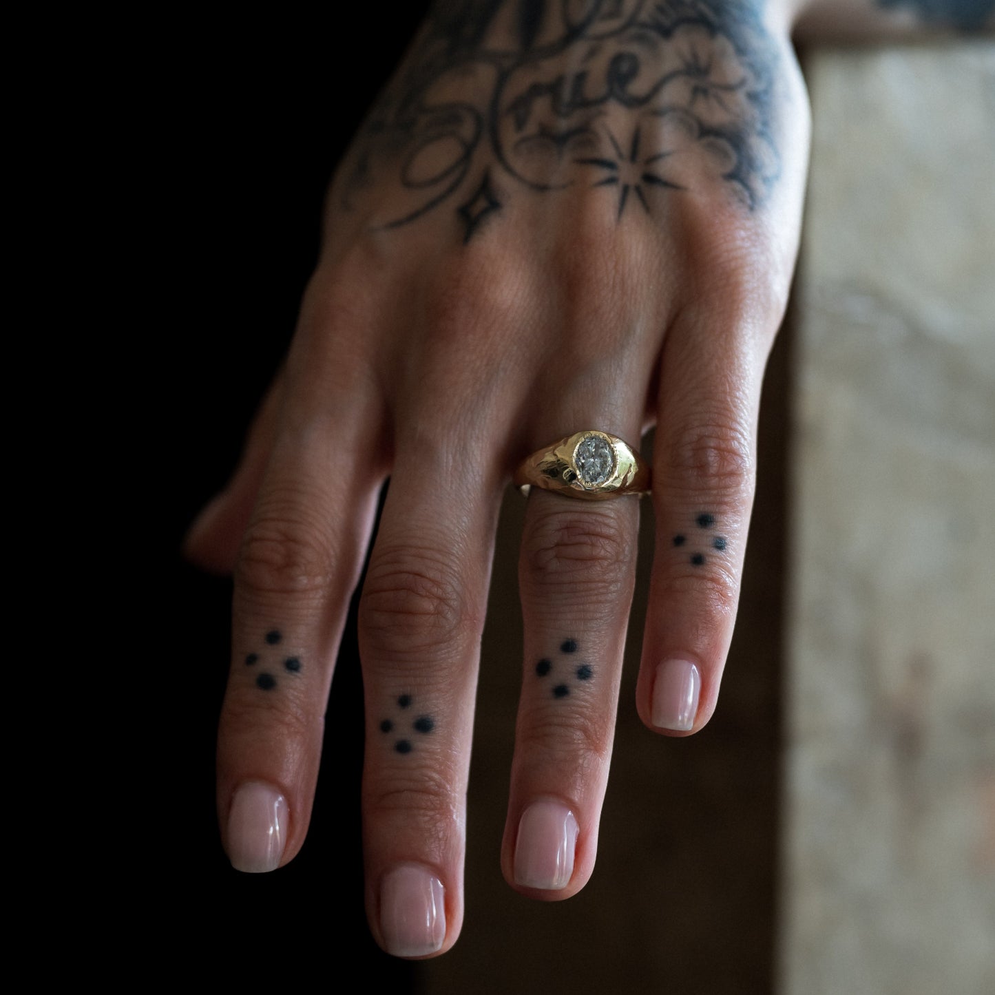 Ellis Mhairi Cameron - Hand with tattoos and a gold ring on a blurred background