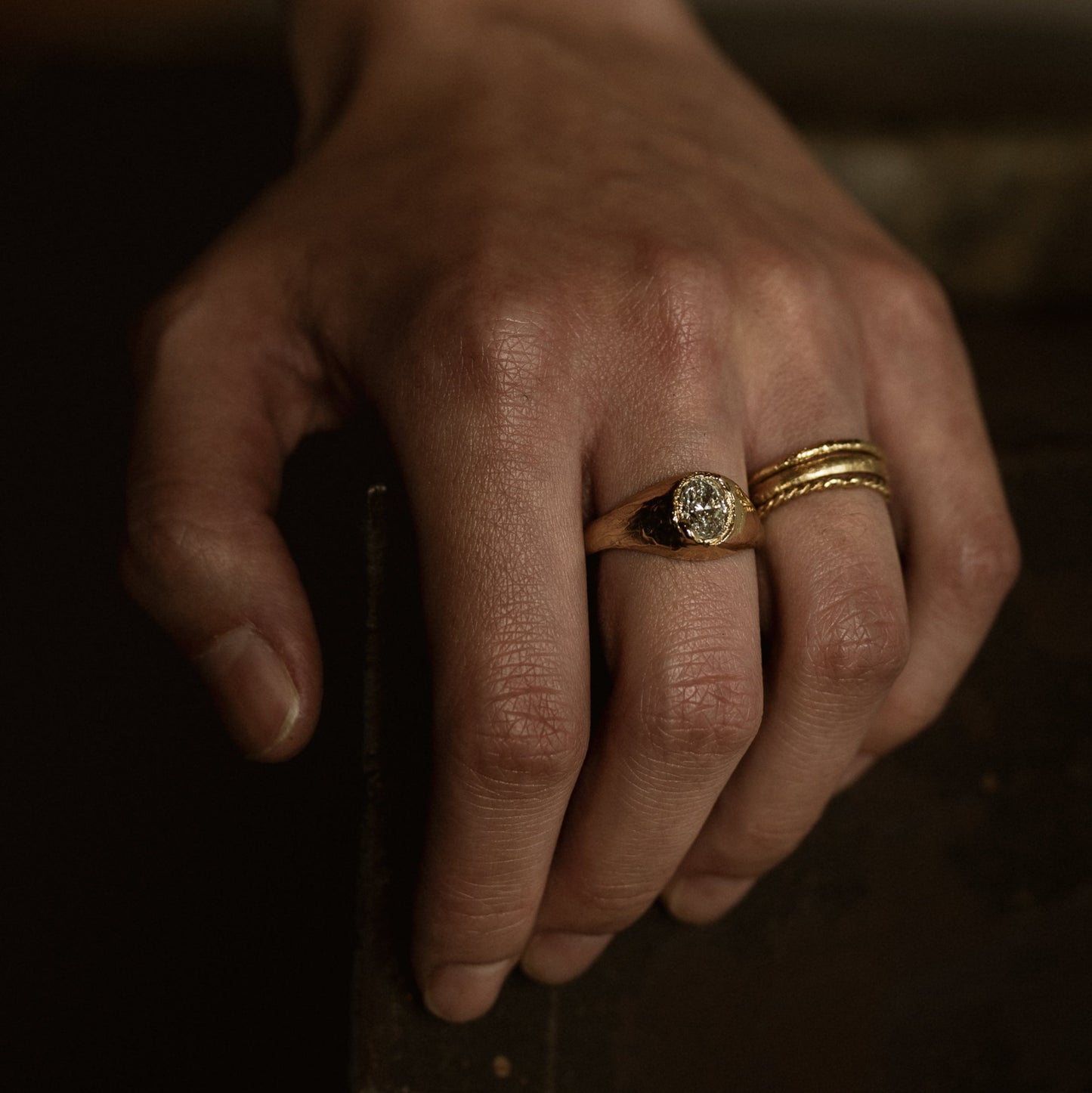 Ellis Mhairi Cameron - Close-up of a hand wearing two gold rings with a dark background