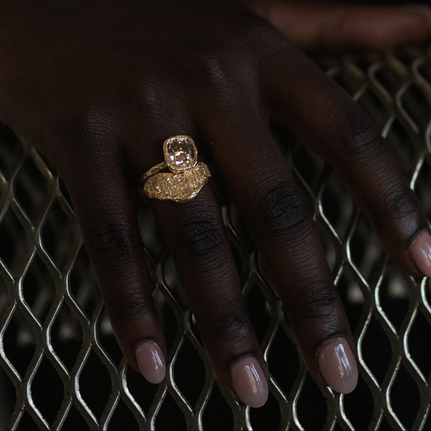 Ellis Mhairi Cameron - Gold ring on a dark-skinned hand against a textured metal background
