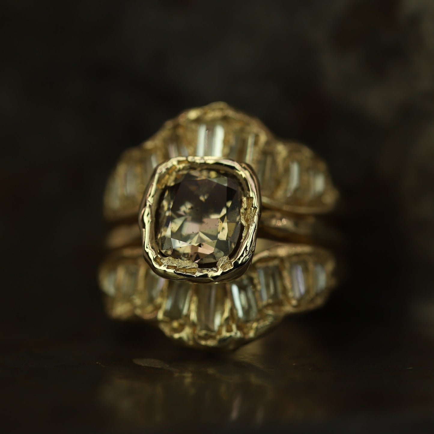 Ellis Mhairi Cameron - Gold ring with a central diamond and smaller diamonds on a dark background