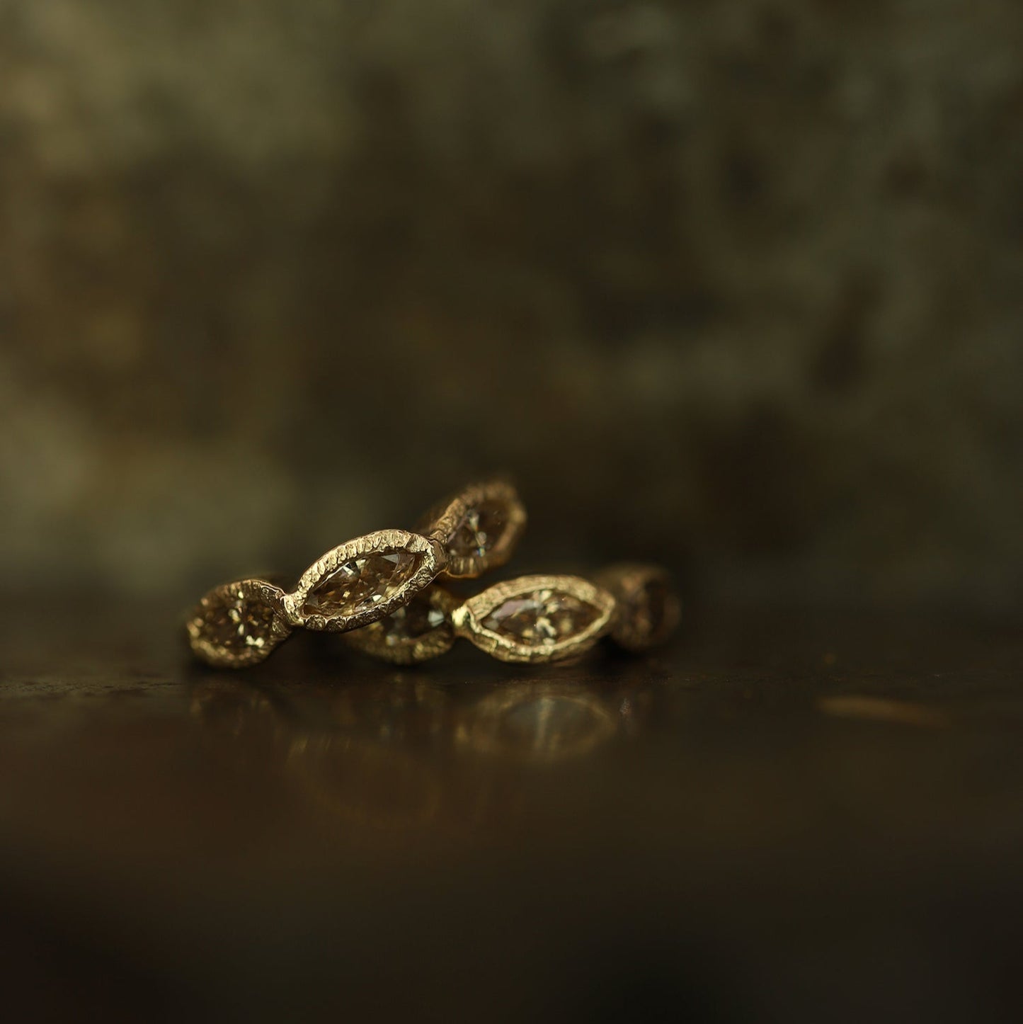 Ellis Mhairi Cameron - Gold earrings on a dark surface with a blurred background