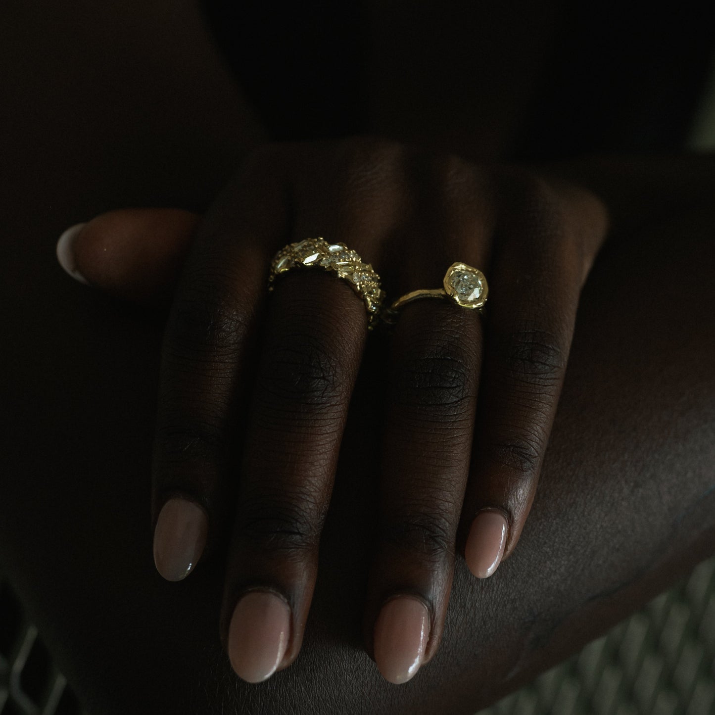 Ellis Mhairi Cameron - Hand wearing a gold ring with a large gemstone on a dark background