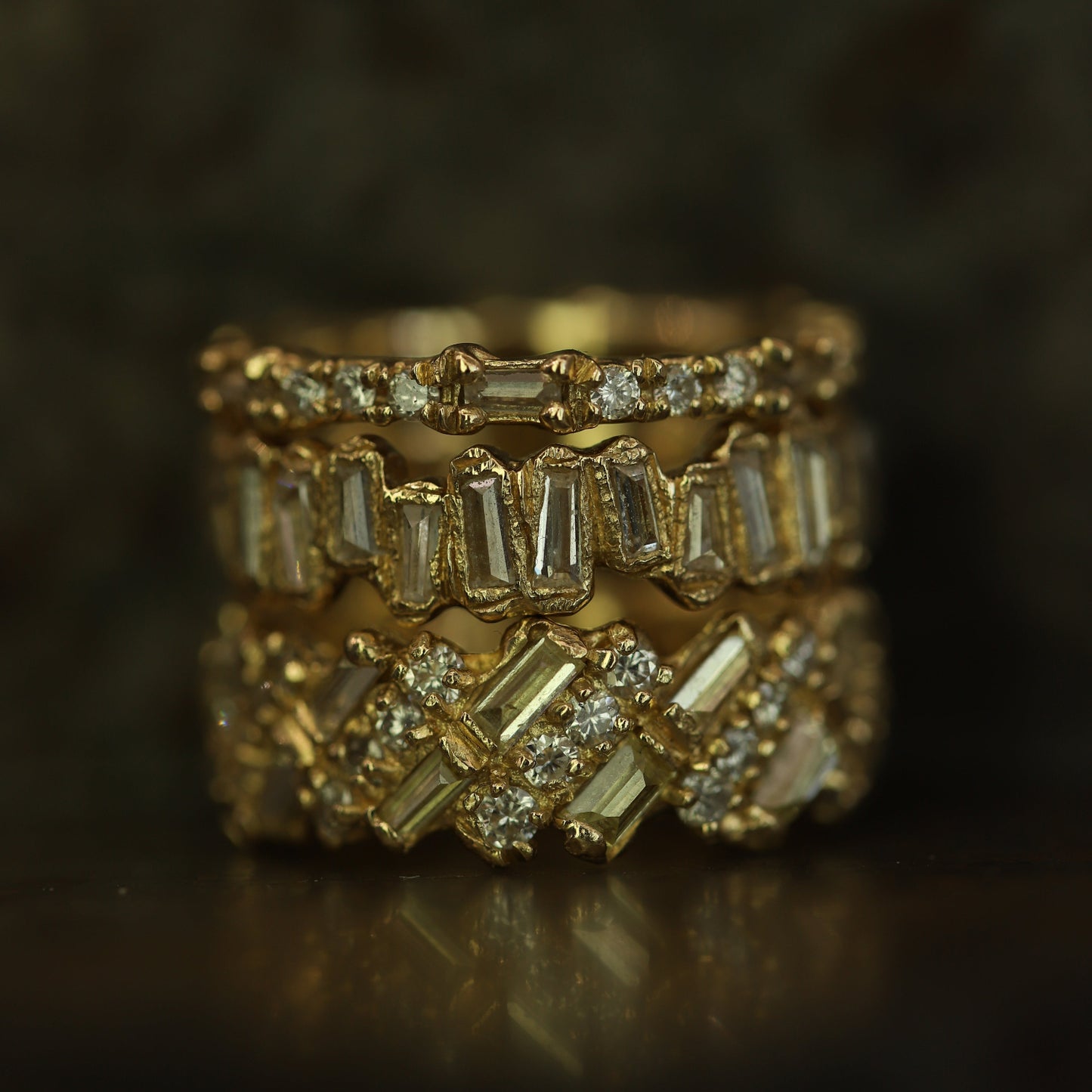 Ellis Mhairi Cameron - Stack of gold rings with diamond accents on a dark background