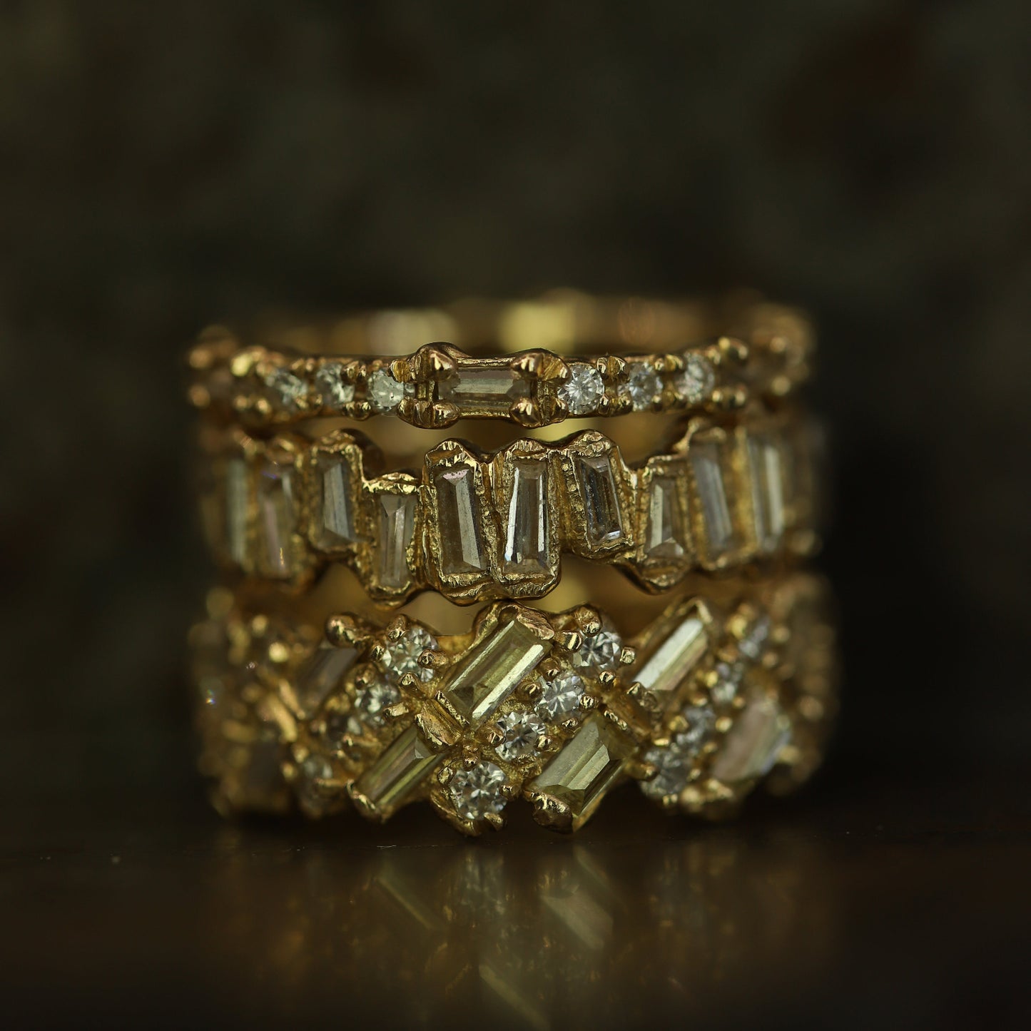 Ellis Mhairi Cameron - Stack of gold rings with diamond accents on a dark background
