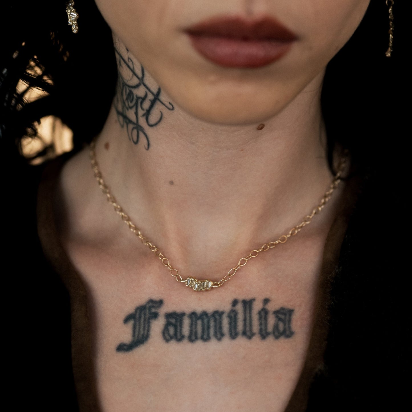 Ellis Mhairi Cameron - Close-up of a person's neck with tattoos and a gold necklace against a dark background