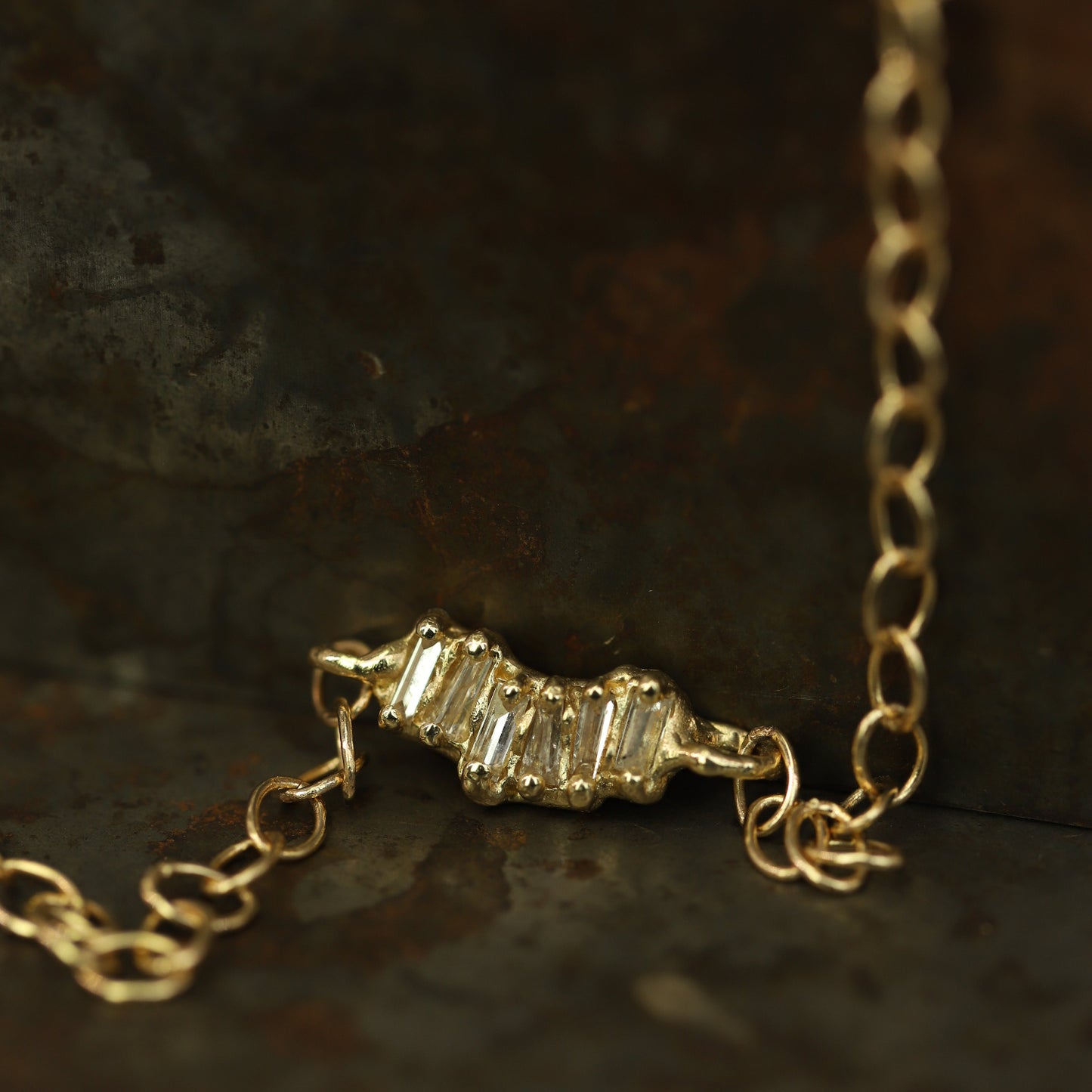 Ellis Mhairi Cameron - Gold necklace with a diamond pendant on a dark surface