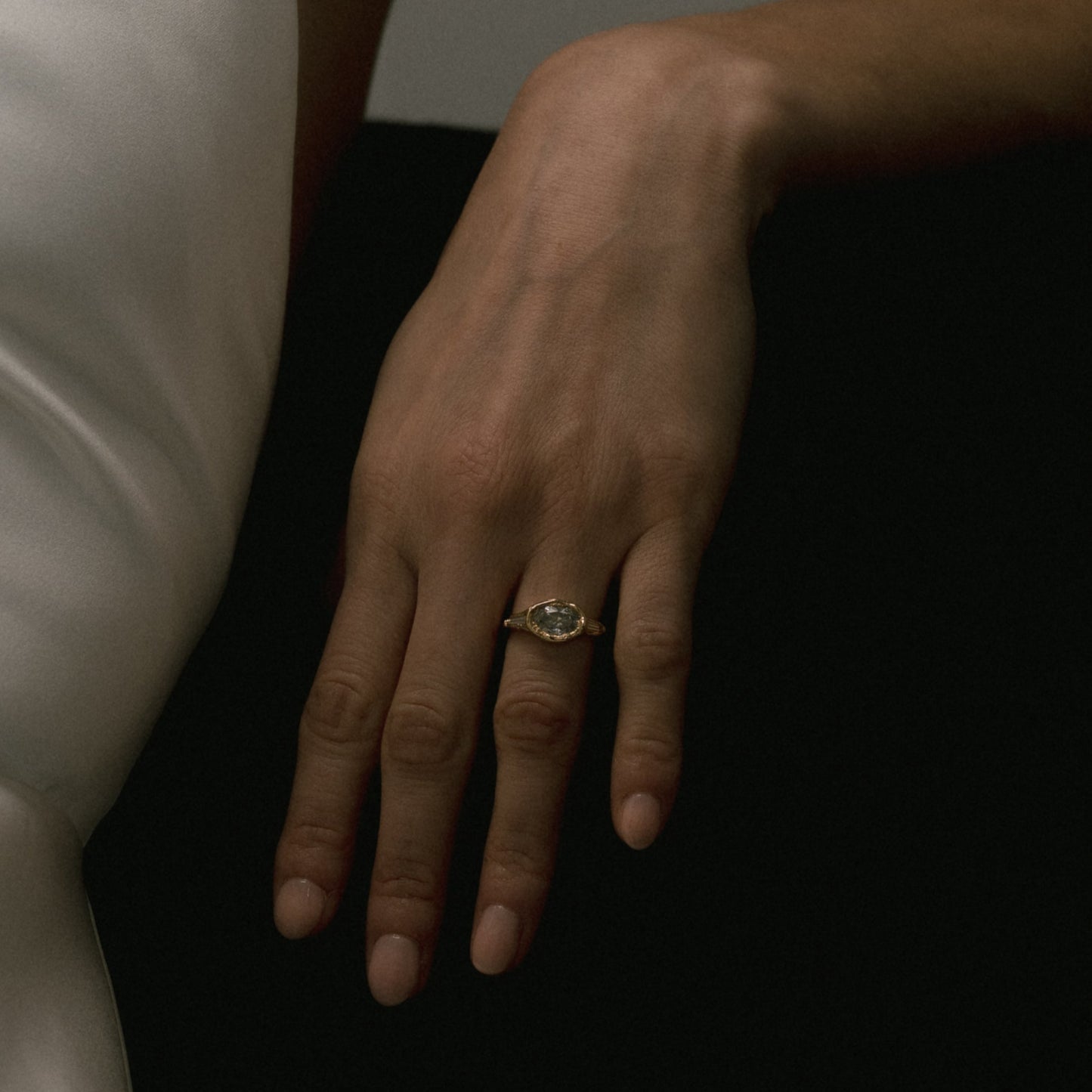 Ellis Mhairi Cameron - Hand wearing a gold ring with a gemstone on a dark background