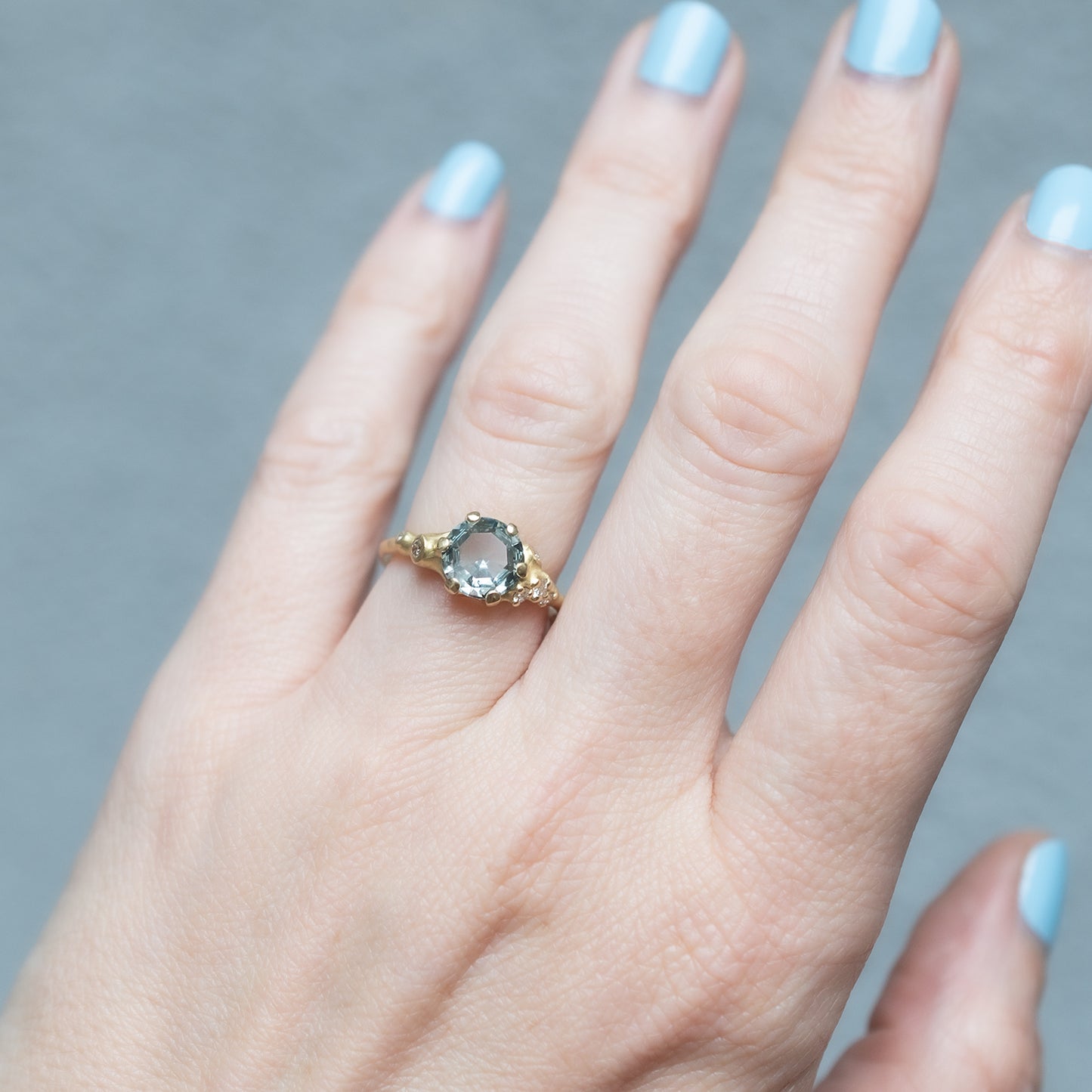 Hand wearing a Johnny Ninos gold ring with a green gemstone against a gray background