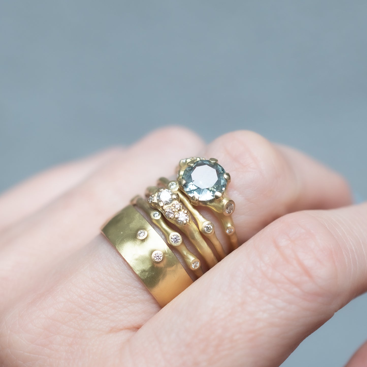Johnny Ninos Gold rings with gemstones on a finger against a gray background