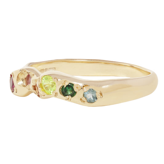 A yellow gold ring featuring four small, round-cut gemstones in a row: a pink stone, a light green stone, a dark green stone, and a light blue stone, set against a plain white background.
