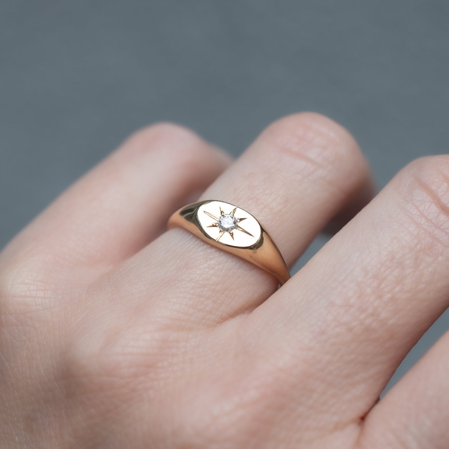 Gold ring with a star design on a person's finger against a gray background
