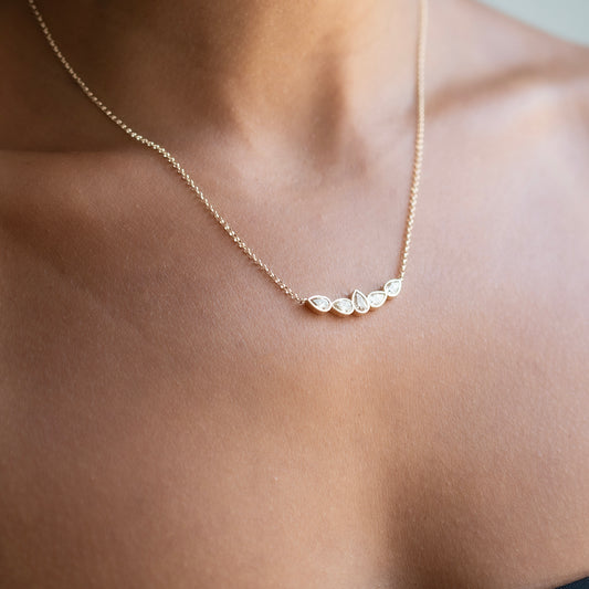 A delicate gold chain necklace with five small champagne diamonds worn on a model's neck.