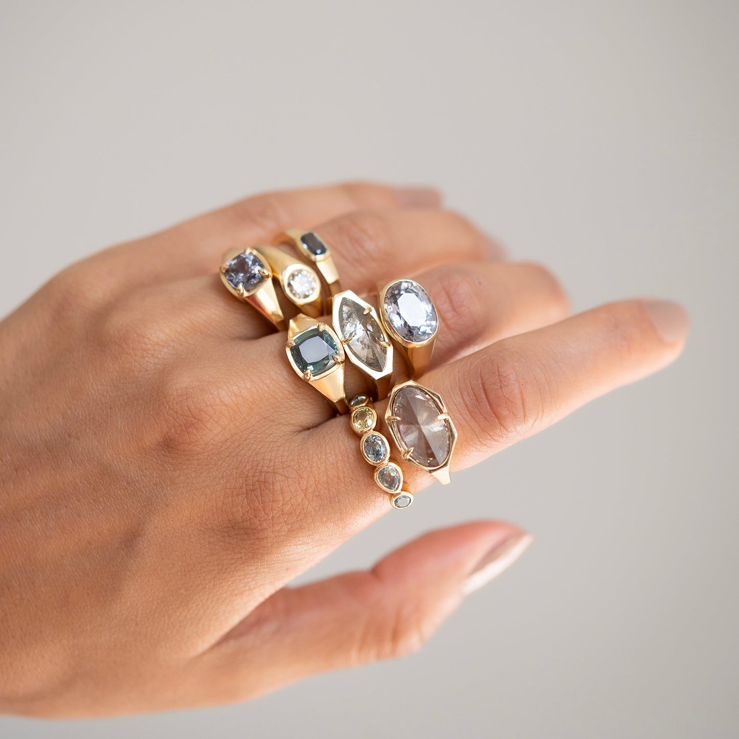 Hand wearing multiple gold rings with gemstones on a neutral background