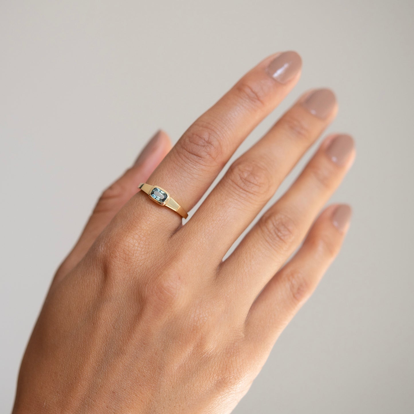 Lauren Wolf - Gold ring with a gemstone on a hand against a neutral background