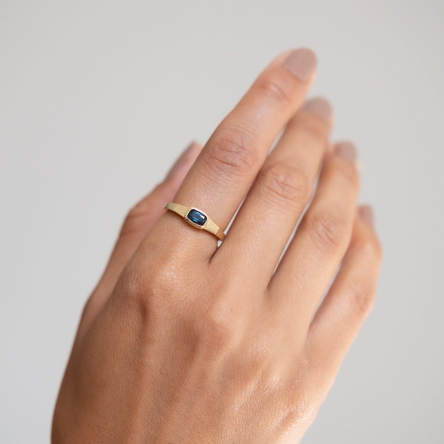 Gold ring with a blue stone on a hand against a plain background