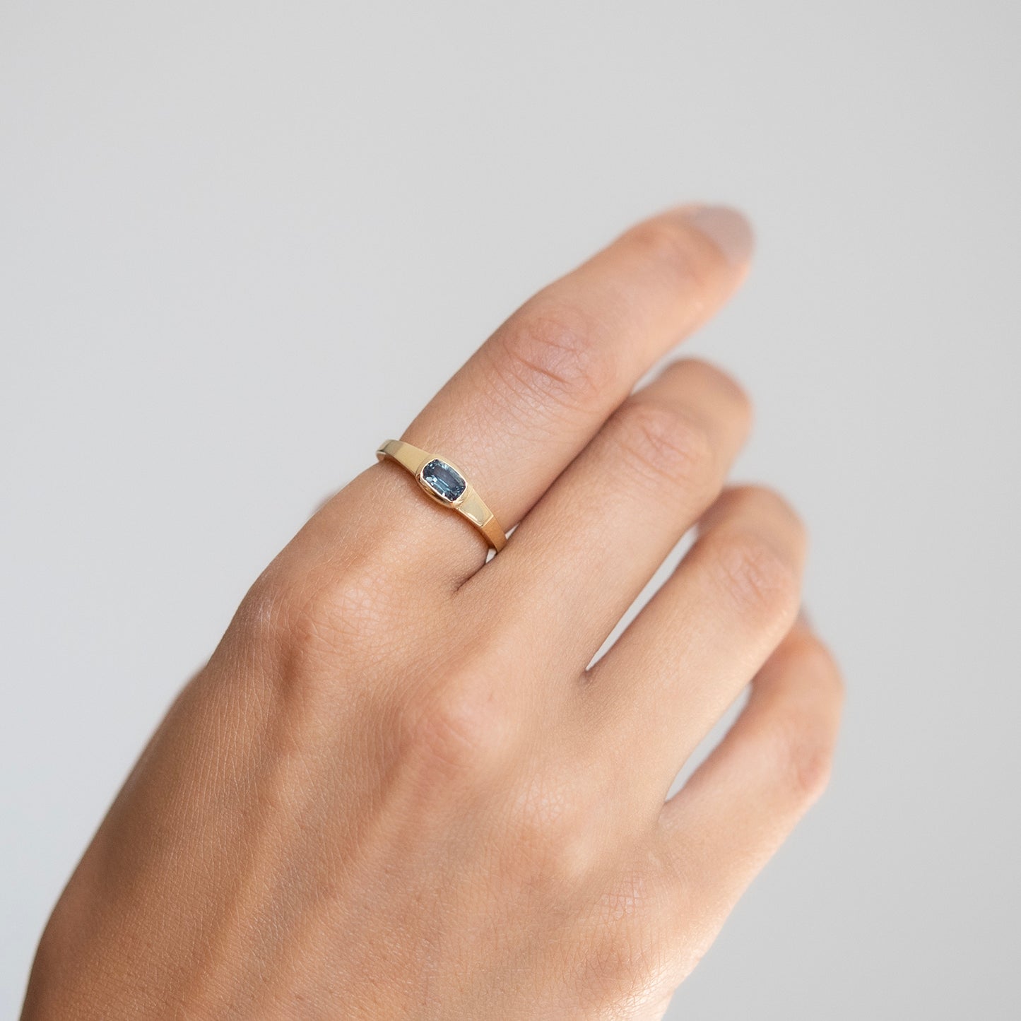 Lauren Wolf - Hand wearing a gold ring with a blue stone on a light gray background