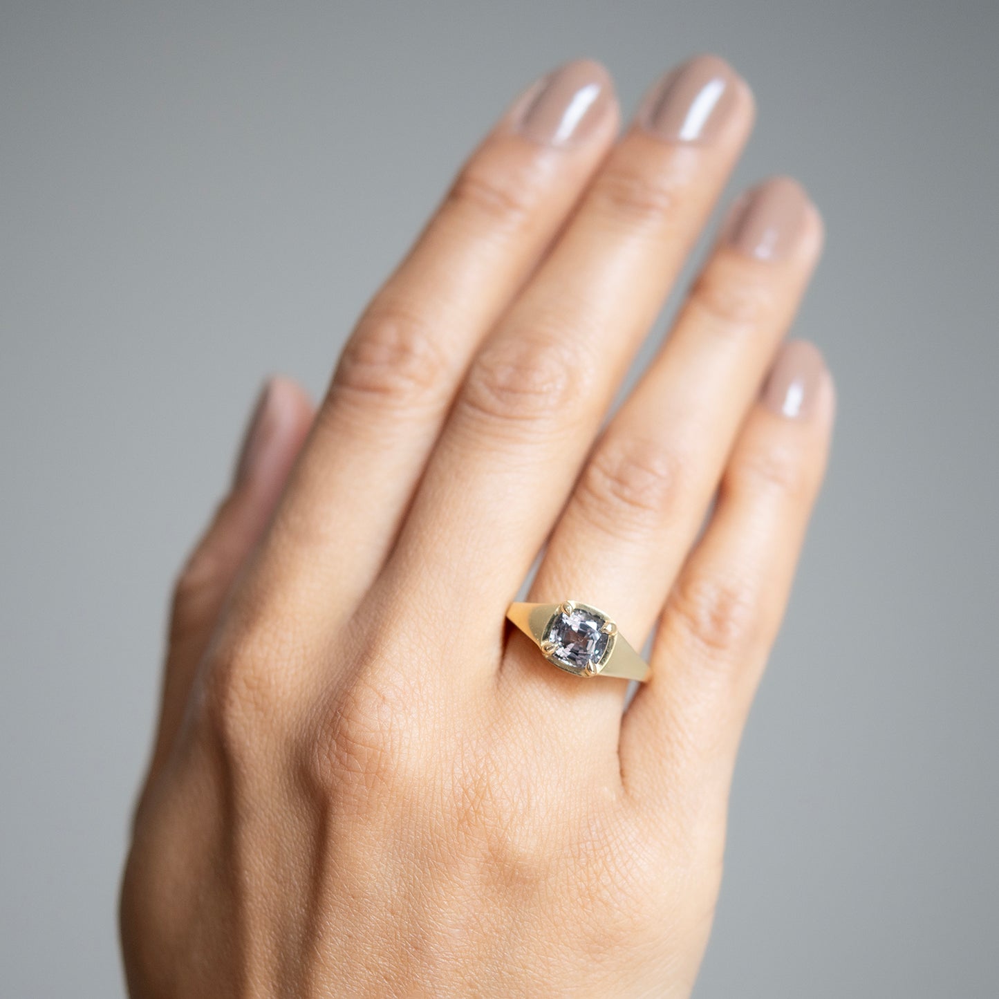 Lauren Wolf - Hand wearing a gold ring with a spinel on a gray background