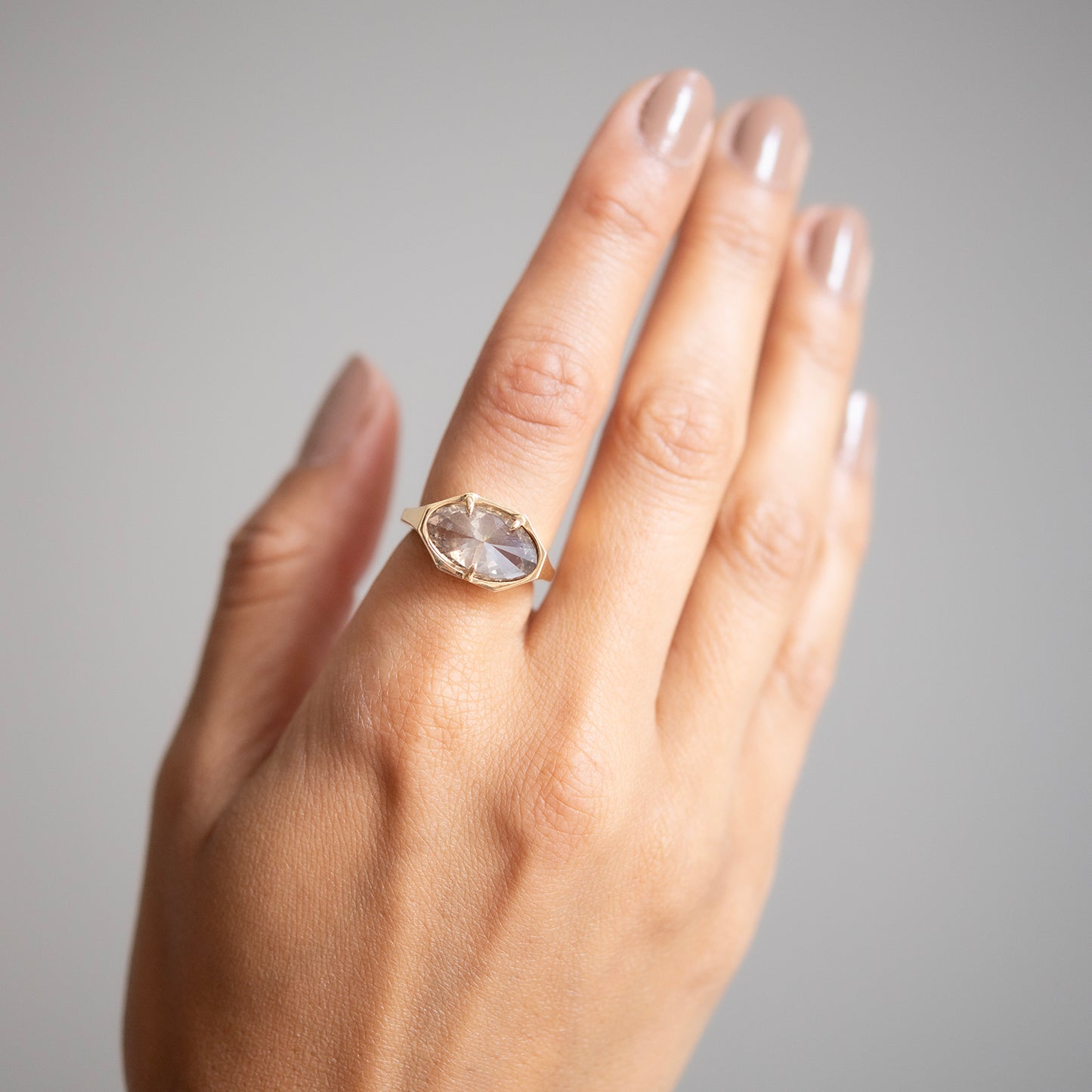 Lauren Wolf - Hand wearing a gold ring with a clear gemstone on a gray background