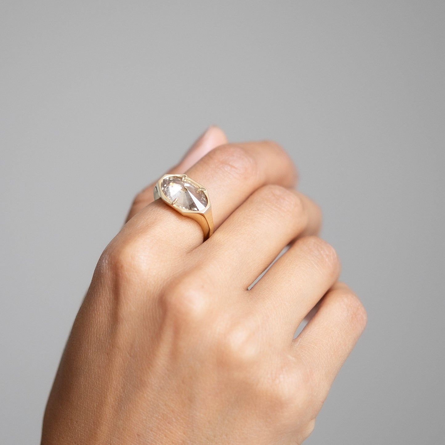 Hand wearing a gold ring with a clear gemstone on a gray background