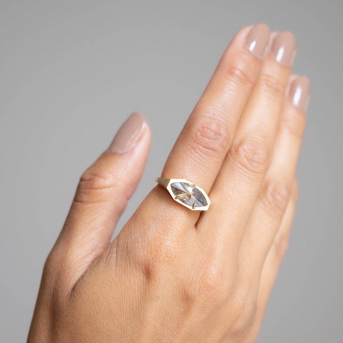 Hand wearing a gold ring with a clear gemstone on a gray background