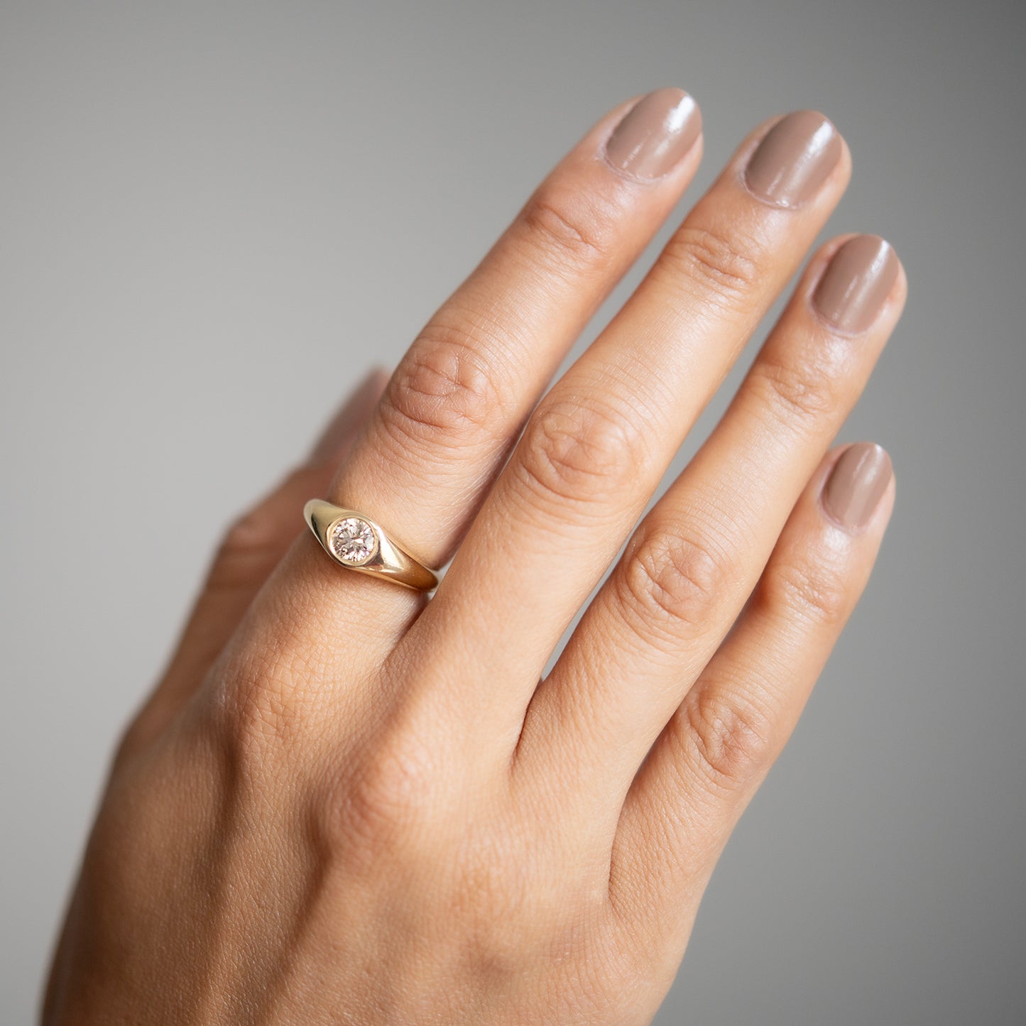 Hand wearing a gold ring with a diamond on a neutral background