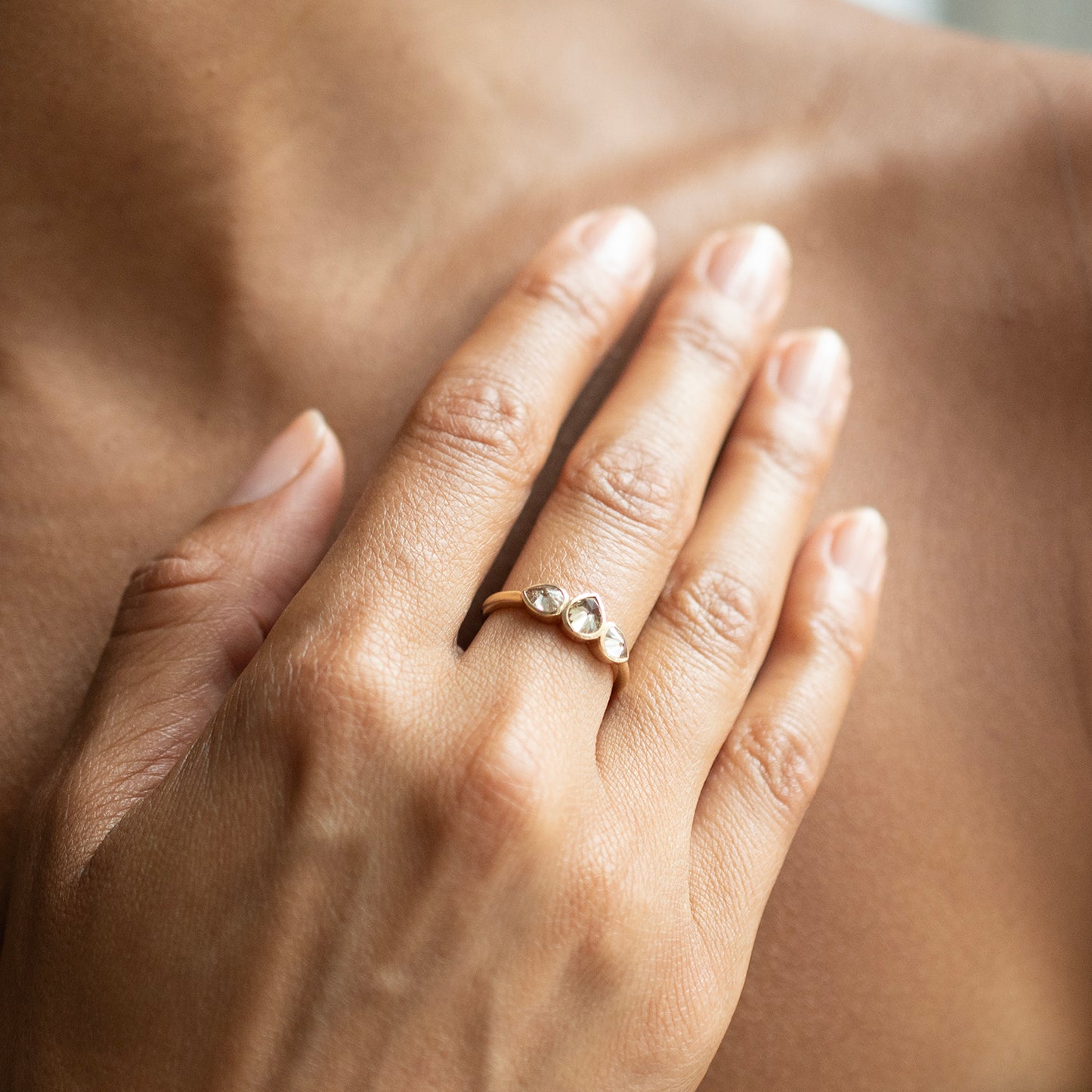 A close-up of a person's hand resting on their chest, wearing a delicate gold ring with two small clear pear-shaped stones.