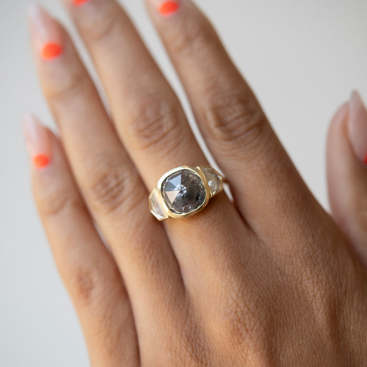 Hand wearing a gold ring with a large diamond on a light background