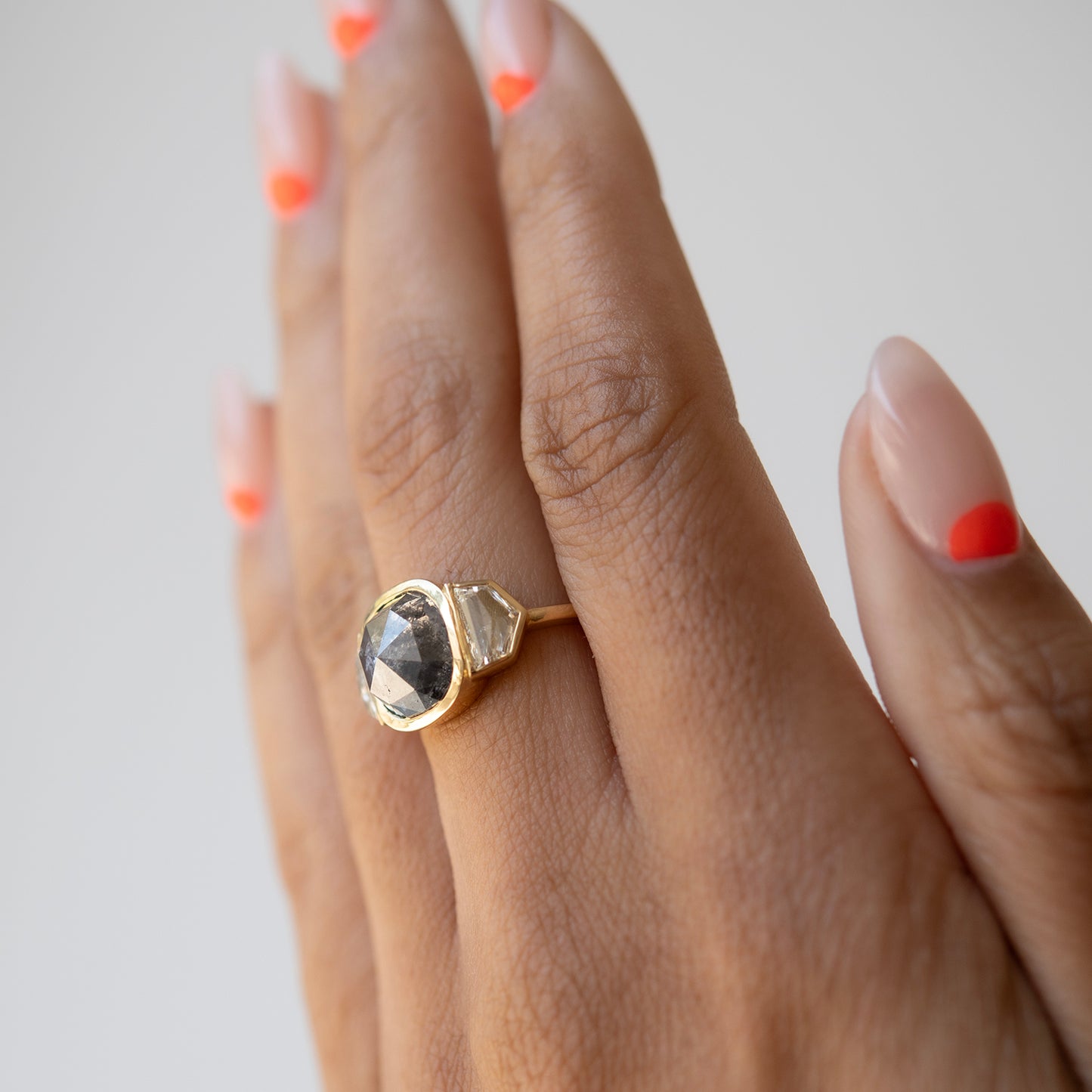 Hand wearing a gold ring with a gemstone on a neutral background