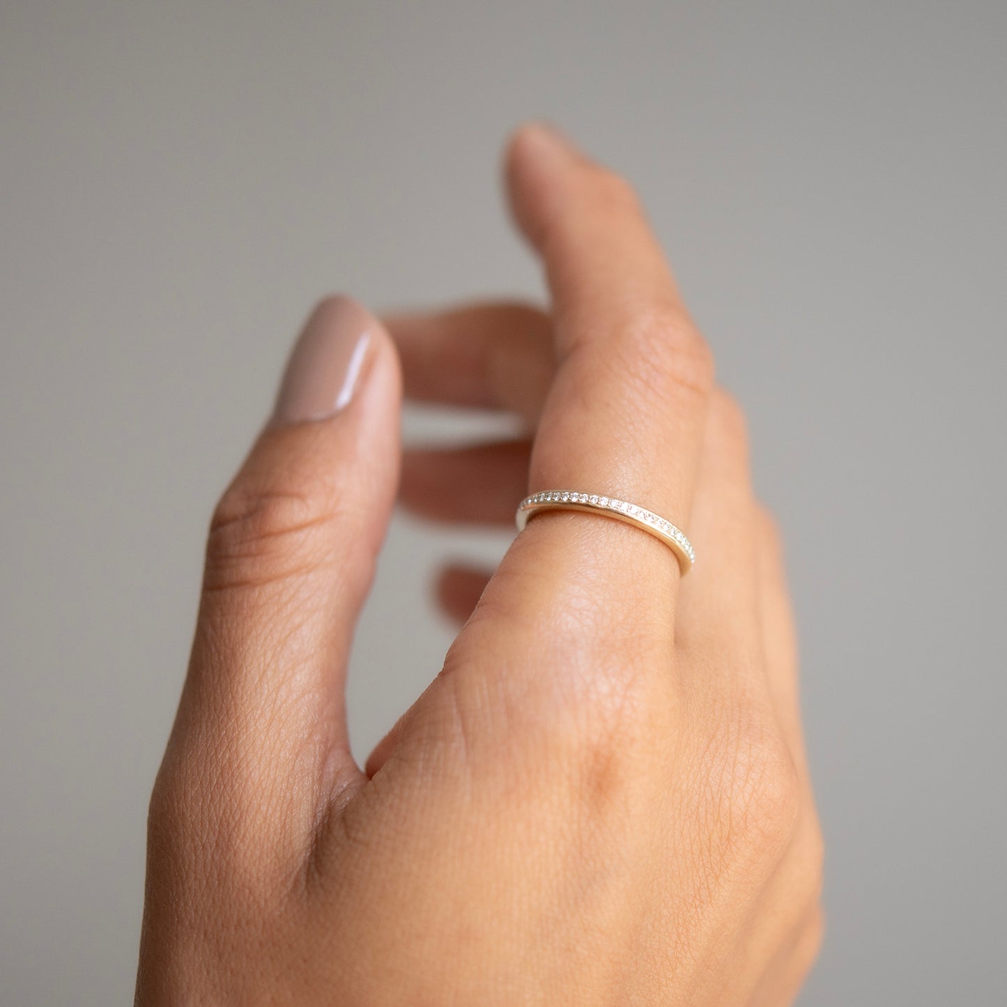 Hand wearing a gold ring on a neutral background
