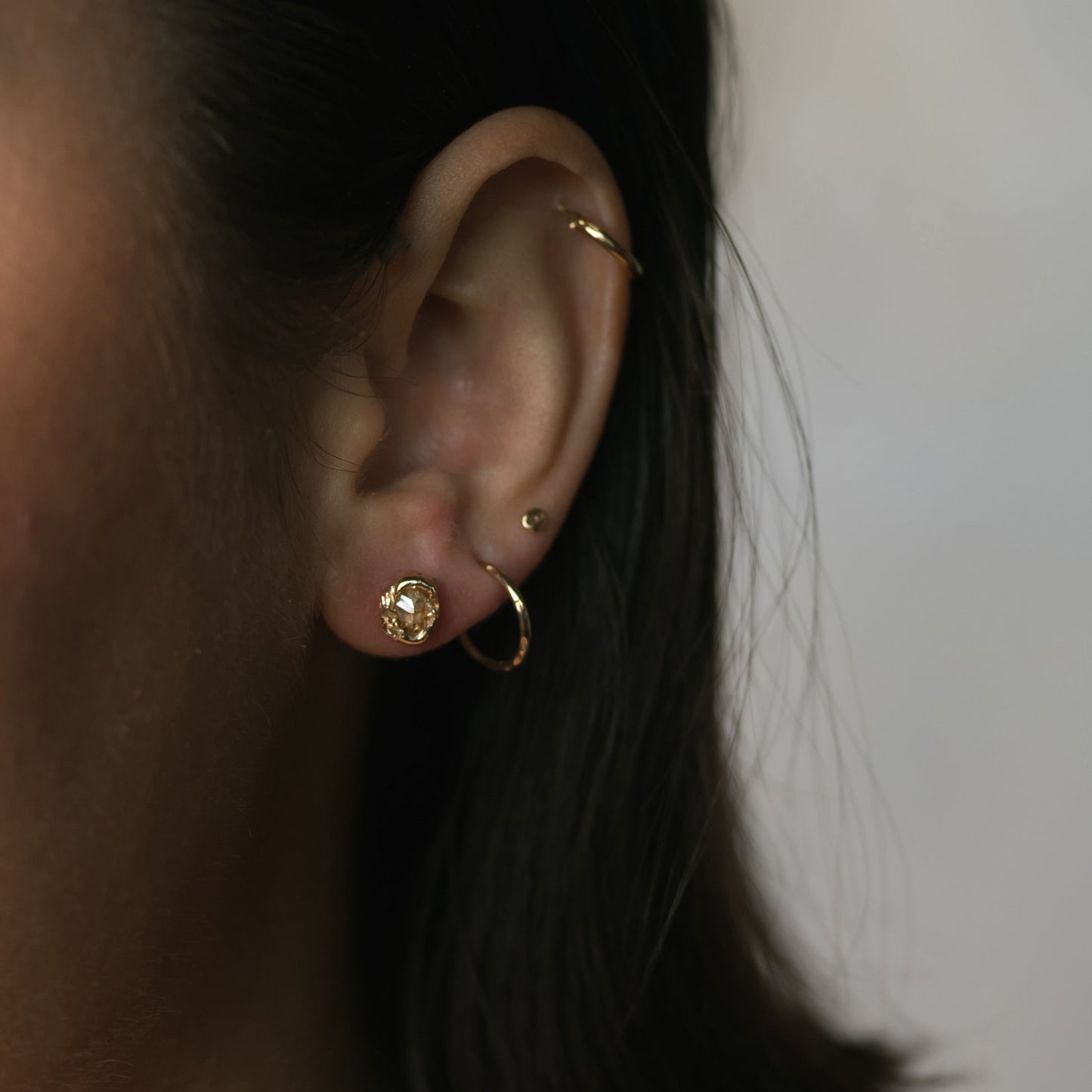 Ellis Mhairi Cameron - Close-up of an ear with gold earrings against a neutral background