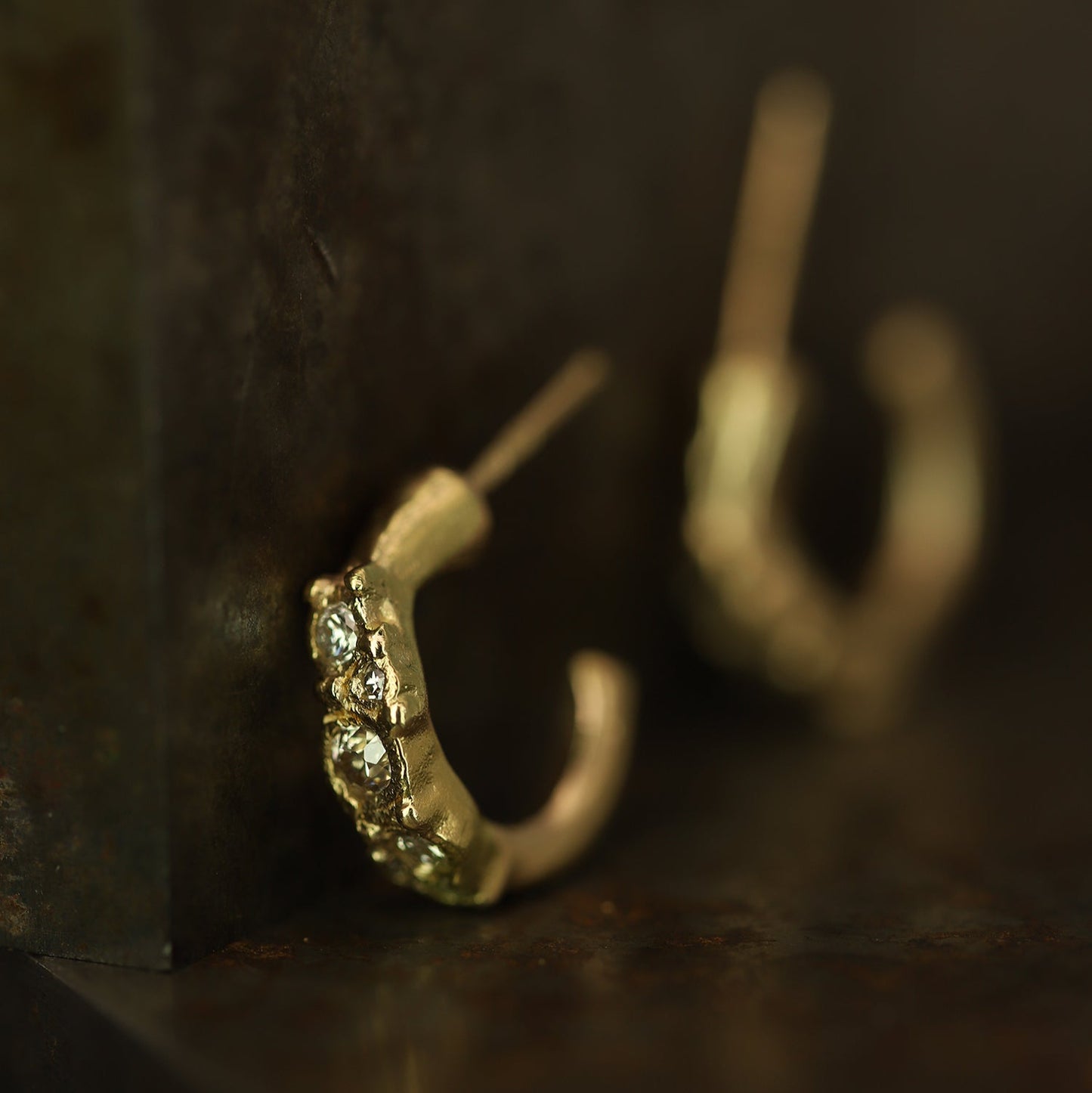 Ellis Mhairi Cameron - Gold hoop earrings with embedded stones on a dark surface