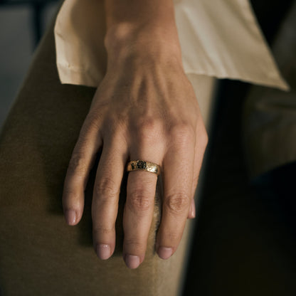 Hand wearing a gold ring with a dark stone, resting on a surface.