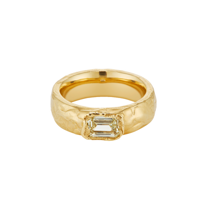 A textured yellow gold ring featuring a rectangular baguette-cut clear gemstone in a bezel setting, shown against a plain white background.