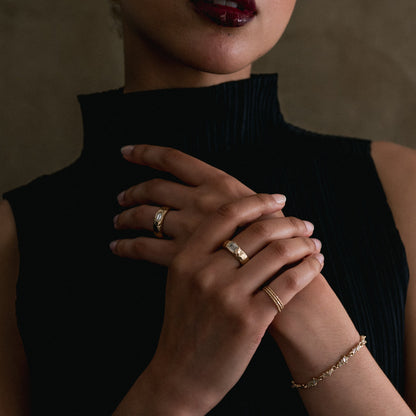 Close-up of a person wearing gold rings and a bracelet on a dark background