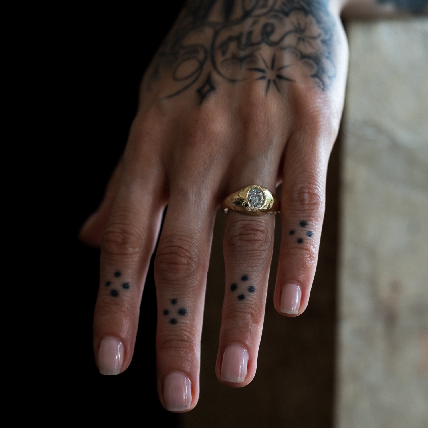 Ellis Mhairi Cameron - Hand with tattoos and a gold ring on a blurred background