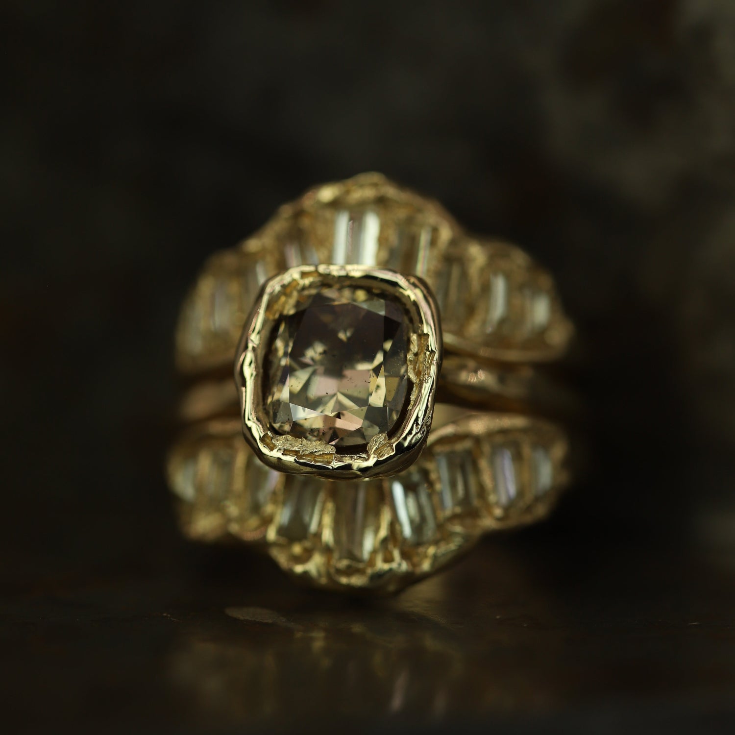 Ellis Mhairi Cameron - Gold ring with a central diamond and smaller diamonds on a dark background