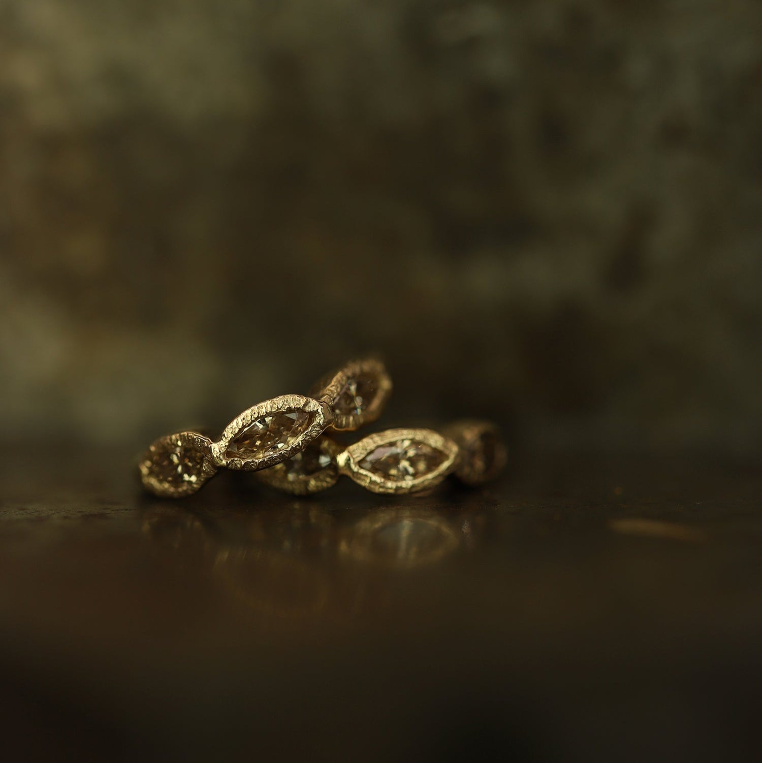 Ellis Mhairi Cameron - Gold earrings on a dark surface with a blurred background