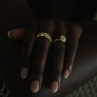 Ellis Mhairi Cameron - Hand wearing a gold ring with a large gemstone on a dark background