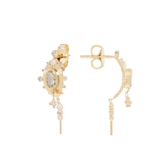 A pair of gold hoop earrings with a central oval green gemstone, surrounded by small clear stones, and featuring dangling chain elements, shown on a plain white background.