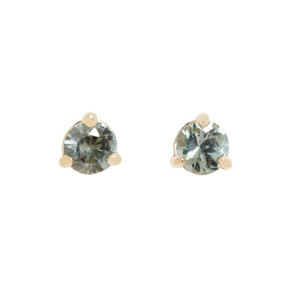 A pair of gold stud earrings with round-cut, faceted gray blue green gemstones, set in a three-prong setting against a plain white background.