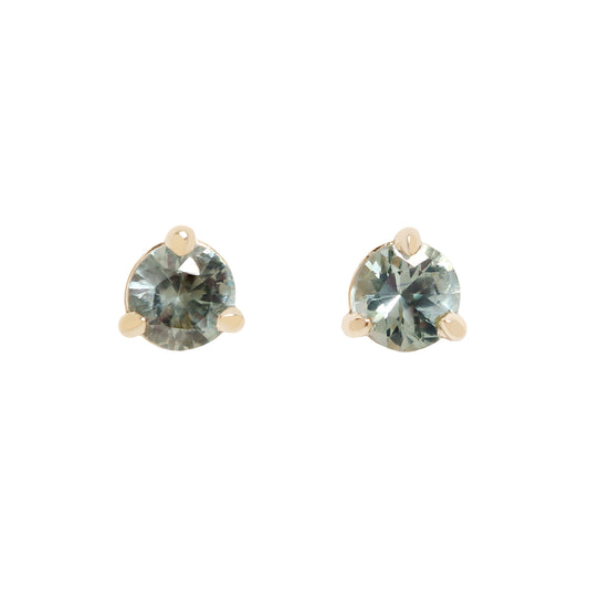 A pair of gold stud earrings with round-cut, faceted gray blue green gemstones, set in a three-prong setting against a plain white background.