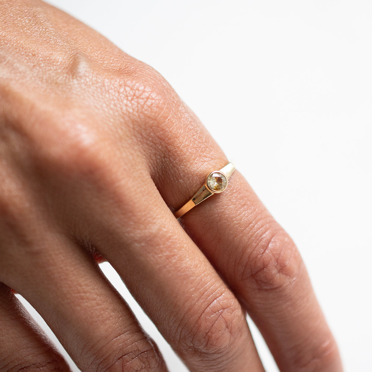 A close-up of a hand wearing a delicate gold ring with a small round sapphire on a plain white background.
