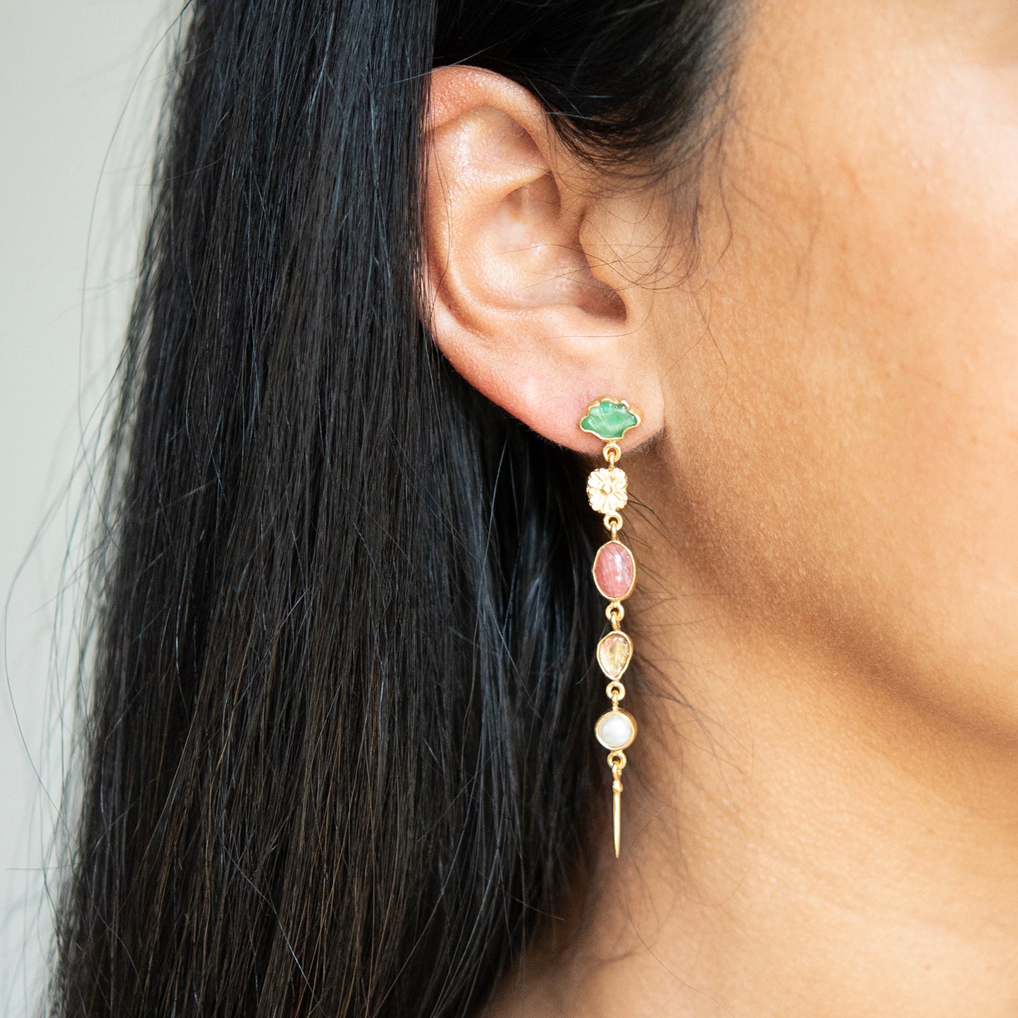 Close-up of an ear wearing a gold earring with gemstones on a neutral background