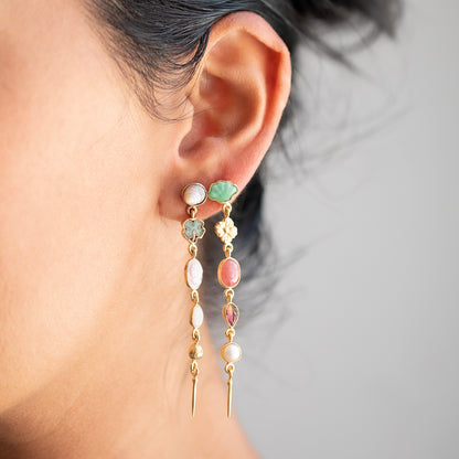 A close-up of a person's ear wearing a pair of gold dangle earrings with pastel green, pink, and white stones.
