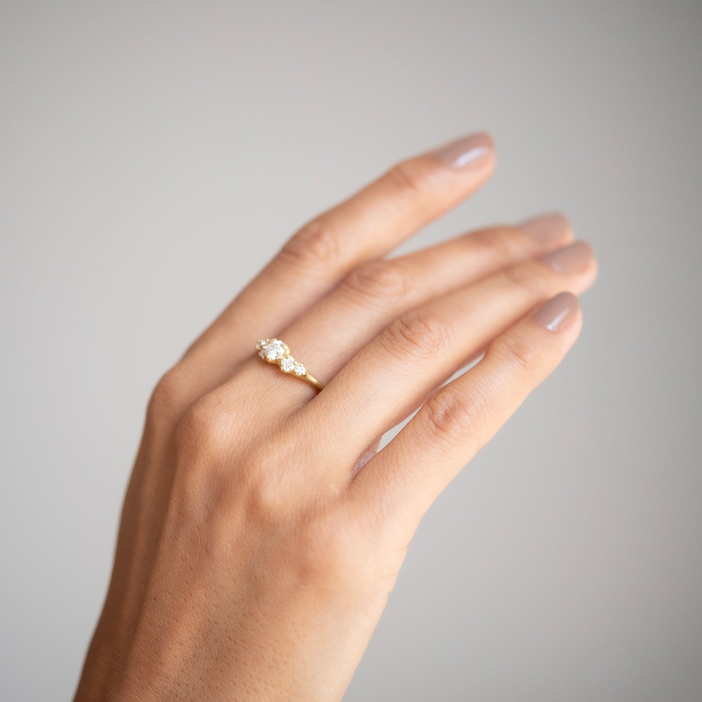 Hand wearing a gold ring with a diamond on a neutral background