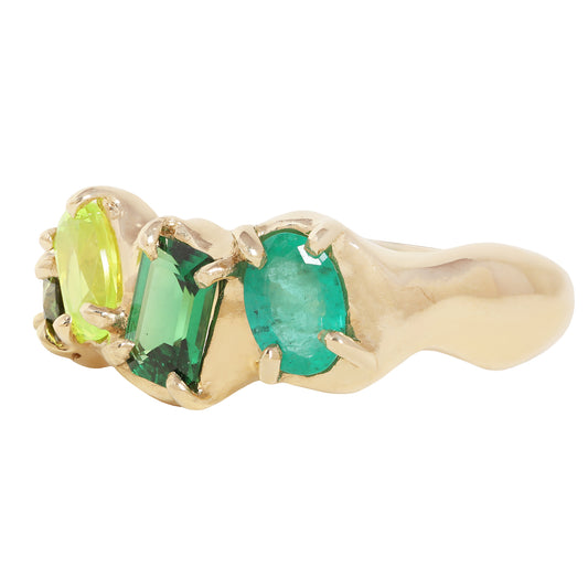 A yellow gold ring featuring three green gemstones in a row: a lime green marquise-cut stone, a rectangular emerald-cut green stone, and a larger oval emerald-cut green stone, all set in a polished gold band against a white background.