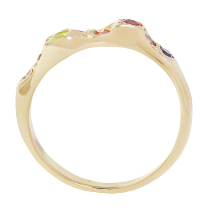 A gold ring with an organic, wavy top setting featuring small multicolored gemstones, shown against a plain white background.