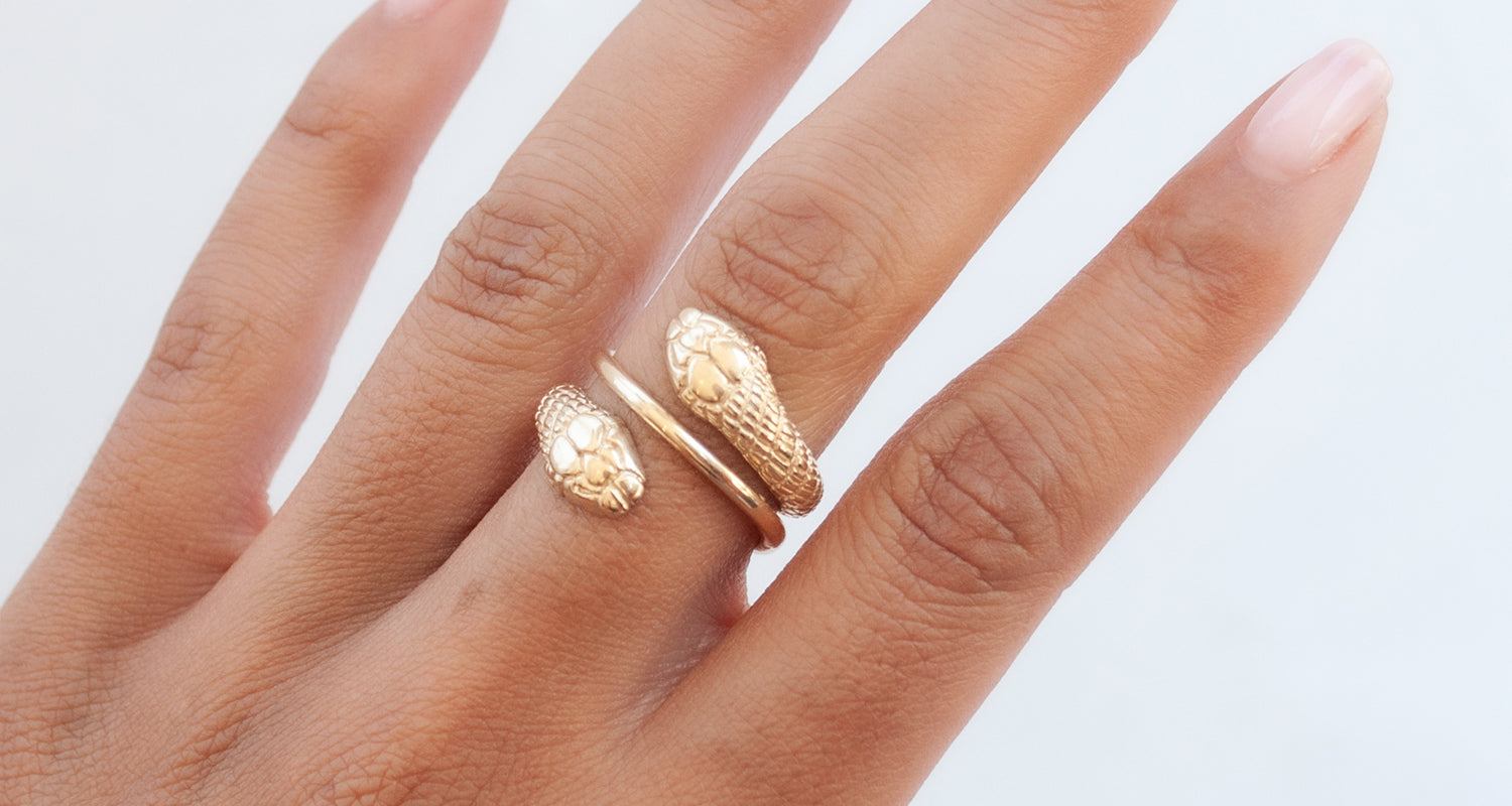 Hand wearing one gold snake ring on a light background
