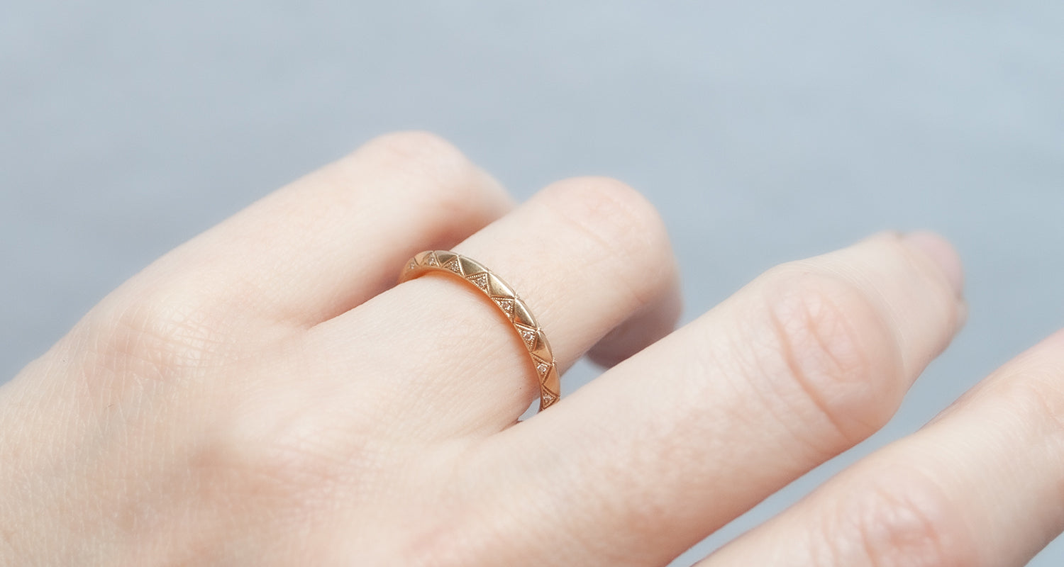Hand wearing a gold ring on a plain background